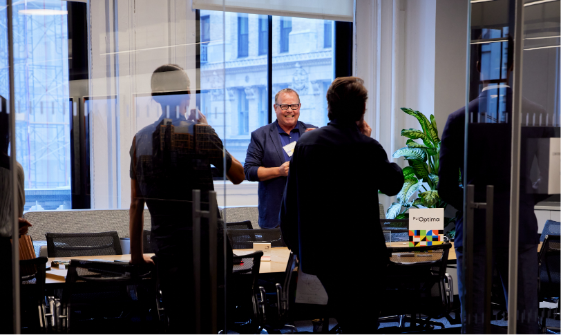 People gathered in a glass-walled conference room having a discussion around a table. People gathered in a glass-walled conference room having a discussion around a table.