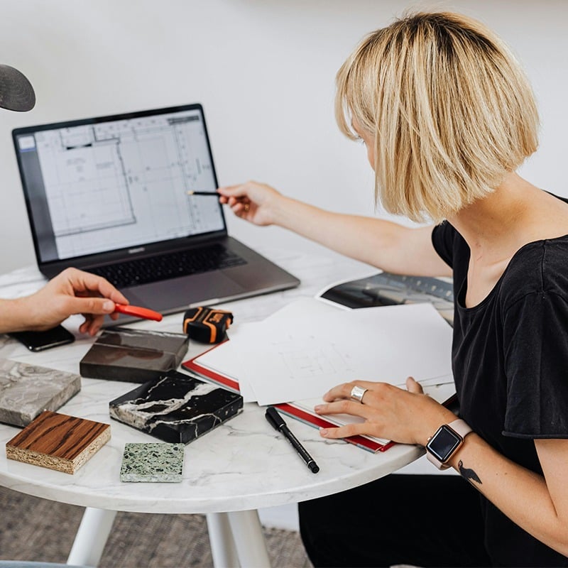 Woman pointing at a laptop while working at a table inside an office setting. Woman pointing at a laptop while working at a table inside an office setting.