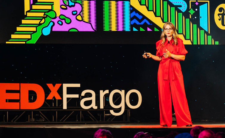 Amanda Schneider delivers a TEDx Talk on a stage. Amanda Schneider delivers a TEDx Talk on a stage.